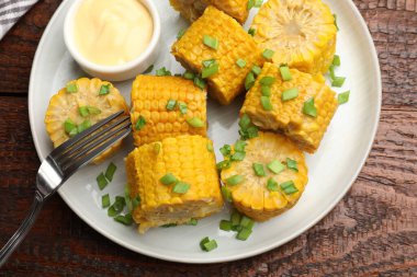 Haşlanmış mısır koçanları ve yeşil soğan ahşap masada servis edilir.