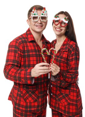 Komik gözlüklü ve pijamalı mutlu çift beyaz arka planda baston şekerlerle kalp yapıyor. Noel atmosferi