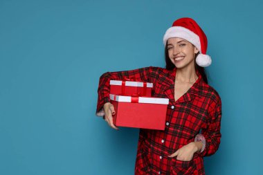 Noel Baba şapkalı mutlu kadın açık mavi arka planda Noel hediyeleri, mesaj için yer