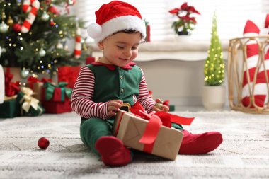 Noel Baba şapkalı küçük çocuk Noel için dekore edilmiş odada yerde hediyeyle