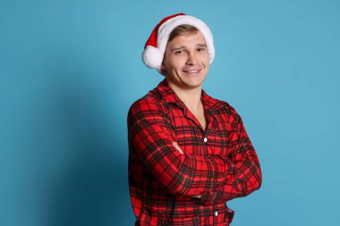 Açık mavi arka planda Noel Baba şapkalı ve pijamalı mutlu bir adam. Noel atmosferi