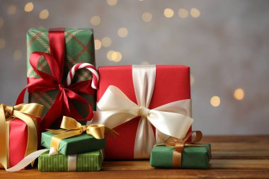 Noel hediyesi kutuları ahşap masanın üzerinde gri arka planda Bokeh ışıkları, yakın plan