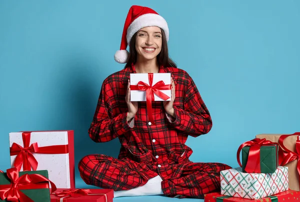 Noel Baba şapkalı ve pijamalı mutlu kadın. Açık mavi arka planda Noel hediyeleri.