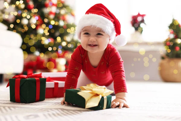 Evde yerde hediyeleri olan Noel Baba şapkalı şirin bir çocuk. Bebeğin ilk Noel 'i