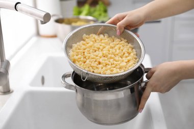 Mutfakta elek ve tencereyle makarna emen kadın, yakın plan.