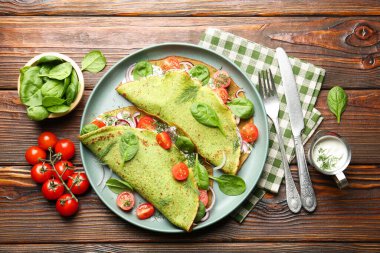 Lezzetli, domatesli ıspanaklı krep, soğanlı, ekşi kremalı ve ahşap masadaki yapraklı, düz.