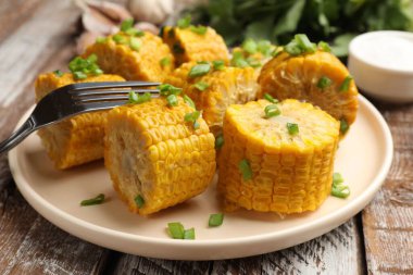 Haşlanmış mısır koçanları ve yeşil soğanlar ahşap masada servis ediliyor.