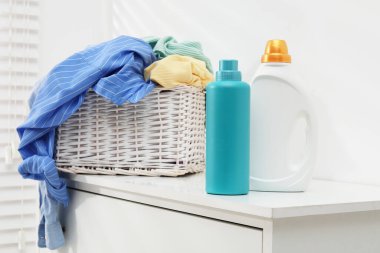 Çamaşır sepetinde giysi ve deterjan var. Beyaz duvarın yanındaki dolapta. Kapalı.