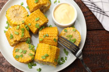 Haşlanmış mısır koçanları ve yeşil soğan ahşap masada servis edilir.