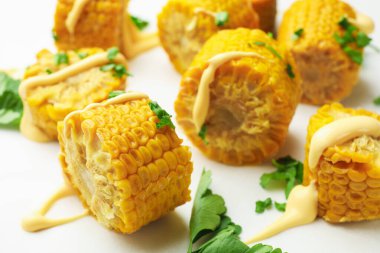 Beyaz masada maydanozlu ve soslu haşlanmış mısır koçanı parçaları.