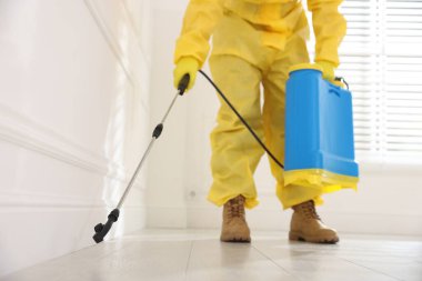 Koruyucu kıyafetli haşereci böcek ilacı sıkıyor, yakın plan.