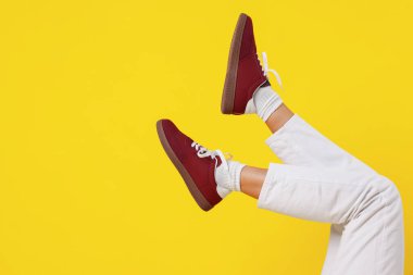 Sarı arka planda şık bordo ayakkabılar giyen bir kadın, yakın plan. Metin için boşluk