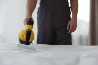 Haşere kontrol işçisi yatağı temizliyor, kapalı alanda buhar temizleyicisiyle, yakın plan