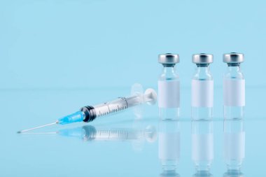 Cam şişelerde aşı ve ayna yüzeyinde turkuaz arka plana karşı şırınga, yakın plan