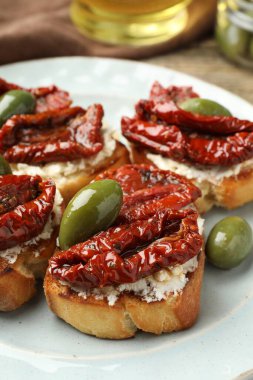 Krem peynirli lezzetli bruschettalar, güneşte kurutulmuş domatesler ve yeşil zeytinler masada, yakın plan.