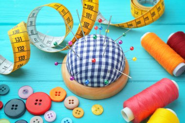 İğneler, iğneler, düğmeler, mezuralar ve açık mavi ahşap masa üzerindeki iplik makaraları ile kareli iğneli iğne.