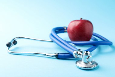 Açık mavi arkaplanda olgun elma ve steteskop, yakın plan.