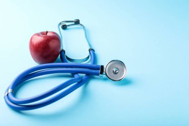 Açık mavi arka planda olgun elma ve steteskop, yakın plan. Metin için boşluk