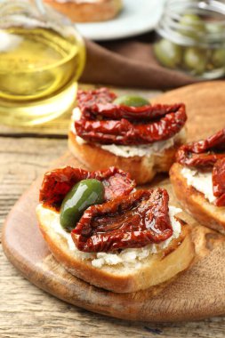 Krem peynirli lezzetli bruschettalar, güneşte kurutulmuş domatesler ve ahşap masada yeşil zeytinler, yakın plan.