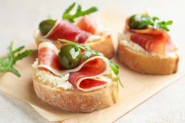 Krem peynirli lezzetli bruschettalar, prosciutto, yeşil zeytin ve roka gri masada, yakın plan.
