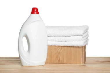 Çamaşır sepeti yumuşak havlular ve ahşap masanın üzerinde beyaz arka planda duran bir şişe deterjan.