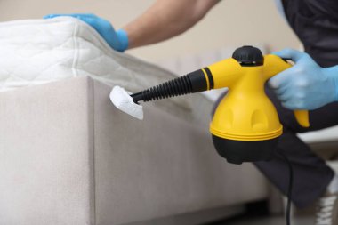 Haşere kontrol işçisi yatağı temizliyor, kapalı alanda buhar temizleyicisiyle, yakın plan