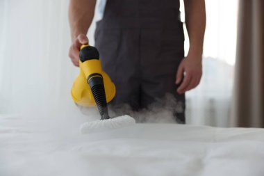 Haşere kontrol işçisi yatağı temizliyor, kapalı alanda buhar temizleyicisiyle, yakın plan