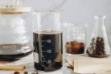 Lezzetli kahve, fasulye, laboratuvar bardağı, kağıt filtreler ve beyaz mermer masada kimya kahve makinesi, yakın plan.