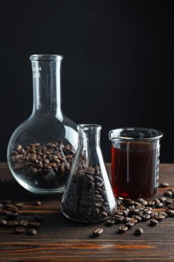 Kahve, fasulye ve beher dolu cam mataralar siyah arka planda, yakın plan.