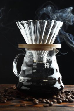 Kahve ve fasulye dumanlı cam kimya kahve makinesi ahşap masada, yakın plan.