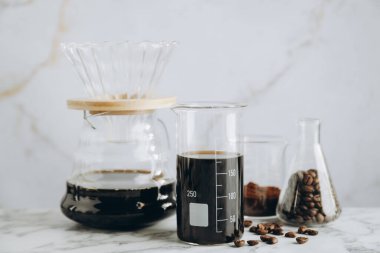 Lezzetli kahve, fasulye, toz, laboratuvar bardağı ve kimya kahve makinesi beyaz mermer masada, yakın plan.