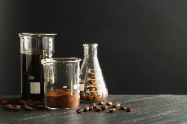 Lezzetli kahve, fasulye ve pudra ile laboratuvar bardakları siyah masada, mesaj için yer var.