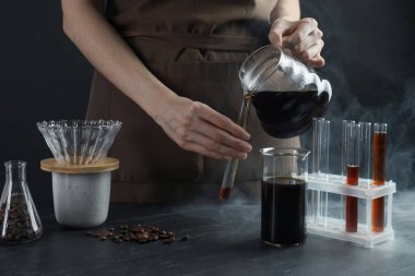 Siyah masada cam test tüpüne damlatan kadın, yakın plan.