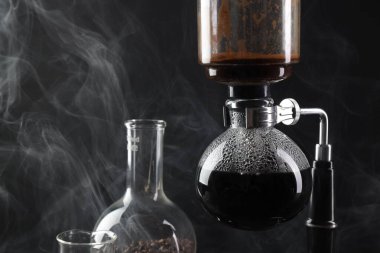 Vakumlu kahve makinesinde aromatik kahve demlemek, laboratuvar bardakları ve siyah arka plandaki fasulyeler, yakın plan.