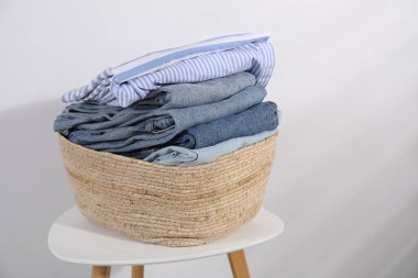 Çamaşır sepetinin içinde beyaz duvarın yanındaki masada giysiler var.