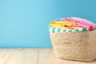 Açık mavi duvarın yanındaki ahşap masada giysileri olan çamaşır sepeti. Metin için boşluk