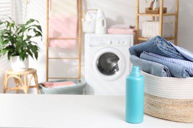 Çamaşır sepeti, içinde giysiler ve beyaz masa üzerinde bir şişe deterjan. Metin için boşluk