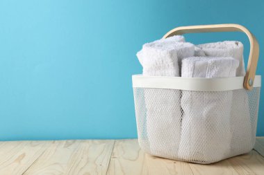 İçerideki açık mavi duvarın yanındaki ahşap masanın üzerinde havlular olan çamaşır sepeti. Metin için boşluk