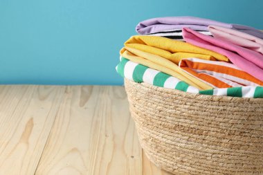 Açık mavi duvarın yanındaki ahşap masada giysileri olan çamaşır sepeti, yakın plan. Metin için boşluk