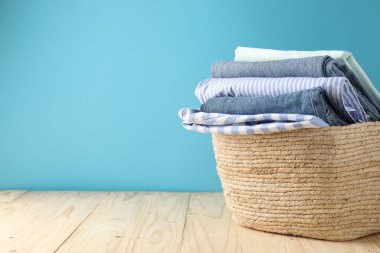 Açık mavi duvarın yanındaki ahşap masada giysileri olan çamaşır sepeti. Metin için boşluk