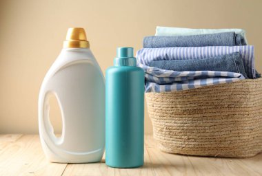 Çamaşır sepetinde giysiler ve şişe deterjan bej duvarın yanındaki ahşap masada.