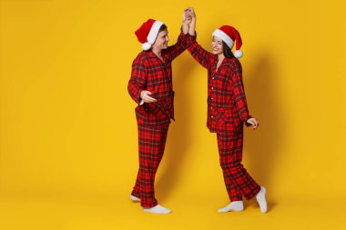 Turuncu arka planda Noel Baba şapkalı ve pijamalı mutlu çift, mesaj için yer var. Noel atmosferi