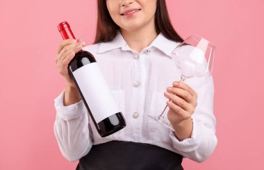 Pembe arka planda kırmızı şarap ve cam şişesi olan profesyonel şarap garsonu.