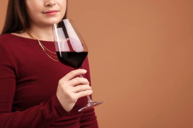 Profesyonel şarap garsonu soluk kahverengi arka planda kırmızı şarap tadıyor, yakın plan. Metin için boşluk