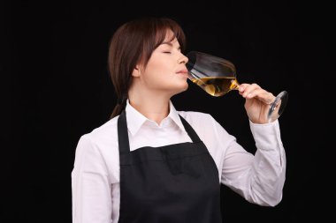 Profesyonel şarap garsonu siyah arka planda beyaz şarap tadıyor.