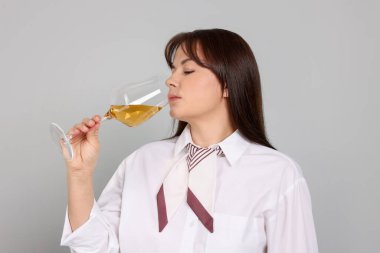 Profesyonel şarap garsonu açık gri arka planda beyaz şarap tadıyor.