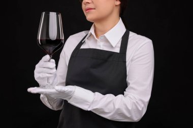 Siyah arka planda kırmızı şarap kadehi olan profesyonel şarap garsonu, yakın plan.