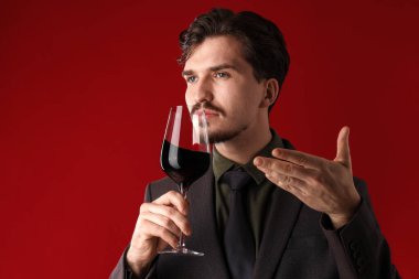 Profesyonel şarap garsonu kırmızı arka planda şarap tadıyor. Metin için boşluk