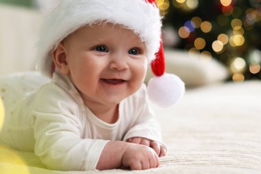 Noel Baba şapkalı şirin bir bebek Noel ışıklarına karşı kanepede, bokeh etkisi