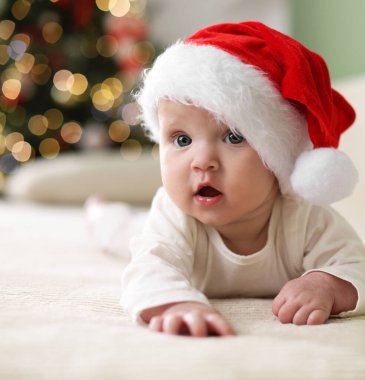 Noel Baba şapkalı şirin bir bebek Noel ışıklarına karşı kanepede, bokeh etkisi